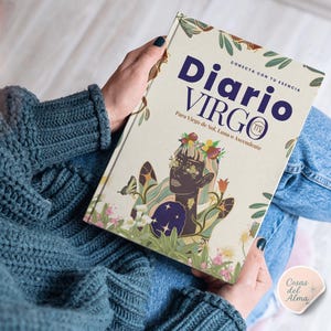 Op de afbeelding: Een dagboek getiteld "Diario Virgo" wordt in handen gehouden. De omslag toont een gestileerde illustratie van een vrouw met bloemen- en vlinderaccenten. De tekst bevat "Conecta con tu Esencia" en "Para Virgo de Sol, Luna o Ascendente."