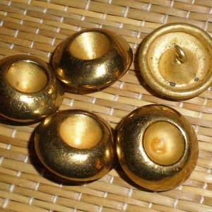 Puede incluir: Cinco botones de metal de color dorado con un centro elevado. Los botones tienen un acabado liso y brillante.
