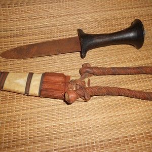 May include: Two knives with wooden handles and leather sheaths. The top knife has a black handle and a rusty blade. The bottom knife has a brown handle and a white bone inlay.