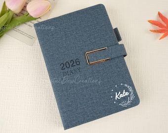 May include: A blue fabric diary for 2026 with a gold-colored clasp. The diary has the word "DIARY" and the year "2026" printed on the front. The name "Kate" is printed on the front with a floral design.