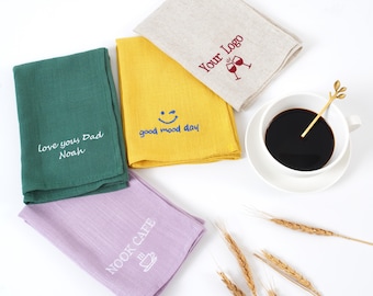 Puede incluir: Vista aérea de cuatro servilletas de lino dobladas en verde, amarillo, lavanda y beige. La servilleta verde tiene el texto "Love you, Dad Noah". La amarilla tiene "good mood day". La beige tiene "Your Logo". También hay una taza de café en la imagen.