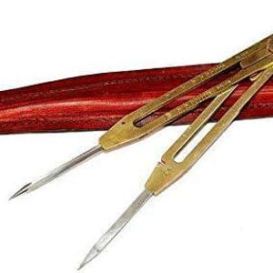 Op de afbeelding: Een vintage messing passer met scherpe punten, rustend op een rode houten koffer. De passer heeft een klassiek ontwerp, met een centraal draaipunt en verstelbare armen. De koffer is lang en smal, met een rijke, roodbruine afwerking.