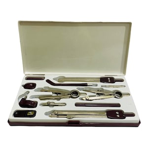 Puede incluir: Un juego de dibujo vintage en un estuche burdeos. El juego incluye varios compases, divisores y otras herramientas de dibujo. Las herramientas son de color plateado con detalles burdeos, cuidadosamente dispuestas en un interior blanco.