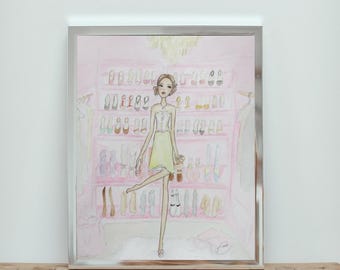 May include: Watercolor illustration of a woman in a yellow dress and heels, posing in front of a pink closet filled with shoes. The artwork is framed in a silver frame and rests on a wooden table.