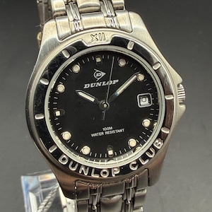 May include: A silver-toned Dunlop Club watch with a black face. The watch features a date display, luminous hands, and the text "100M Water Resistant." The watch band is made of silver-toned metal.