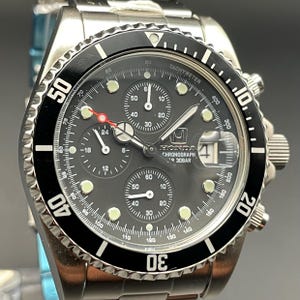 May include: A stainless steel Honda Chronograph watch with a black dial and bezel. The watch features multiple sub-dials, a date display, and luminous markers. The bezel has a tachymeter scale. The watch is water resistant to 30 bar.
