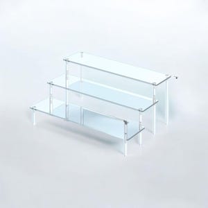 May include: A clear, three-tiered display stand with a stepped design. Each level is a rectangular shelf supported by clear, vertical legs. The stand is made of transparent acrylic, offering a modern and minimalist aesthetic. Ideal for showcasing small items.