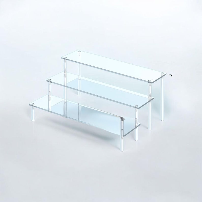 May include: A clear, three-tiered display stand with a stepped design. Each level is a rectangular shelf supported by clear, vertical legs. The stand is made of transparent acrylic, offering a modern and minimalist aesthetic. Ideal for showcasing small items.