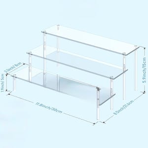 May include: A clear, three-tiered acrylic display stand. The stand is 11.8 inches (30 cm) long, 8.5 inches (21.6 cm) wide, and 5.9 inches (15 cm) tall. Each shelf is supported by clear legs, creating a floating effect. Ideal for showcasing small items.