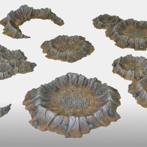 May include: A selection of miniature terrain pieces in shades of brown, grey, and tan. The set includes various shapes, such as craters and archways, suitable for tabletop gaming or model landscapes. The pieces have a weathered appearance.