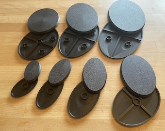 Könnte beinhalten: Eine Sammlung von sieben schwarzen, ovalen Kunststoff-Präsentationssockeln in verschiedenen Größen. Jeder Sockel besteht aus einem strukturierten, massiven ovalen Oberteil und einer glatten, hohlen Unterseite mit integrierten Befestigungspunkten.