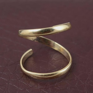May include: A gold-colored ring with a spiral design. The ring curves around the finger, creating a unique and modern look. The ring is made of a shiny, metallic material.
