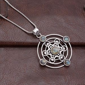 May include: A silver pendant necklace with a geometric design, a central stone, and four smaller stones. The necklace has a fine chain. The background is a brown leather surface.