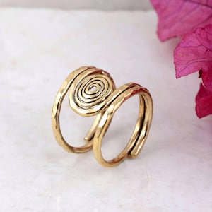 Könnte beinhalten: Ein goldfarbener Ring mit einem Spiraldesign. Der Ring hat eine gehämmerten Textur und ein Doppelband-Design. Die Spirale ist auf der Oberseite des Rings zentriert. Der Ring ist aus Metall.