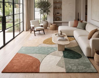 May include: A large rectangular area rug featuring an abstract geometric pattern with overlapping shapes in shades of terracotta, sage green, mustard yellow, and cream, laid out on a light-toned wooden floor in a living room setting.