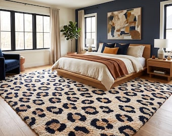 Pode incluir: Um tapete retangular com um padrão de leopardo repetitivo em azul-marinho escuro e bege sobre um fundo creme. O tapete tem um pelo espesso e texturizado, posicionado num quarto com uma estrutura de cama e móveis de madeira.