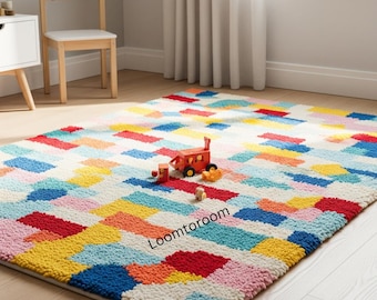May include: A rectangular area rug featuring a multi-colored block pattern in shades of red, blue, yellow, orange, and pink. The rug has a textured, tufted surface and displays the text Loomtoroom in black letters on its surface.