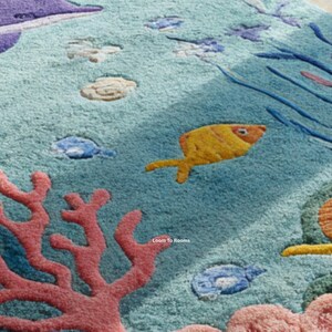 Puede incluir: Primer plano de una alfombra con tem&aacute;tica submarina. La alfombra presenta un fondo azul claro con varias criaturas marinas, incluyendo un pez amarillo, coral y otra vida marina. El dise&ntilde;o es colorido y texturizado.