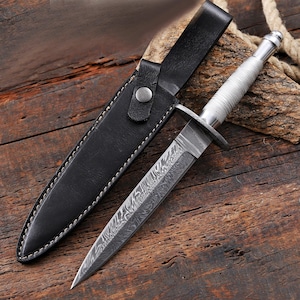 Peut inclure: Un poignard à double tranchant doté d'une lame en acier damas à motifs et d'un manche en métal argenté texturé. Le couteau est accompagné d'un étui en cuir noir avec des coutures blanches et une fermeture à bouton-pression en métal.