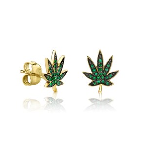 Puede incluir: Un par de pendientes dorados con forma de hojas de cannabis. Cada hoja está detallada con pequeñas piedras preciosas verdes brillantes y delineadas en negro. Los pendientes se muestran sobre un fondo blanco.