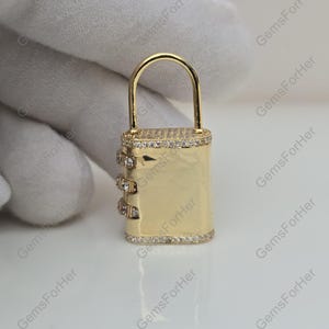 May include: A gold-colored combination lock with a curved handle. The lock is rectangular with a series of three number dials on the side. The top and bottom edges, as well as the dials, are encrusted with small, clear gemstones. The lock is held against a white background.