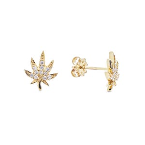 May include: A pair of gold stud earrings shaped like cannabis leaves. Each earring features a polished gold finish and is encrusted with small, clear, round-cut white stones arranged along the surface of the leaf design, complete with a post back.