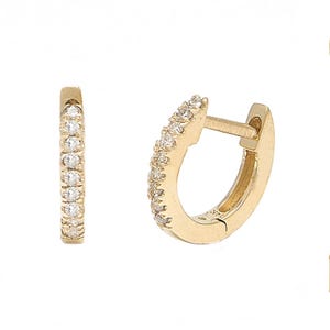 Puede incluir: Un par de pendientes de aro dorados, cada uno incrustado con pequeñas piedras preciosas transparentes. Los pendientes se presentan sobre un fondo blanco, resaltando su diseño y brillo. Los aros son un estilo de joyería clásico.