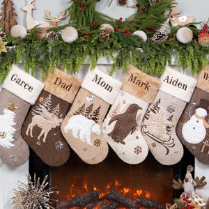 May include: A set of six personalized Christmas stockings with names embroidered on the cuff. Each stocking features a different winter-themed design, including a Christmas tree, deer, polar bear, penguin, and snowman. The stockings are displayed above a fireplace.