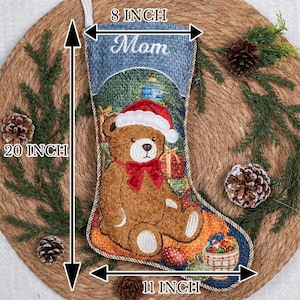 May include: A Christmas stocking featuring a brown teddy bear wearing a red Santa hat and a red bow, with the text "Mom" at the top. The stocking measures 20 inches in height, 8 inches at the top opening, and 11 inches at the widest bottom point.