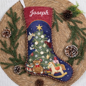 May include: A red and blue Christmas stocking featuring the name Joseph embroidered in white at the top. The stocking displays a decorated green Christmas tree, a brown teddy bear, a rocking horse, and gift boxes on a dark blue background.