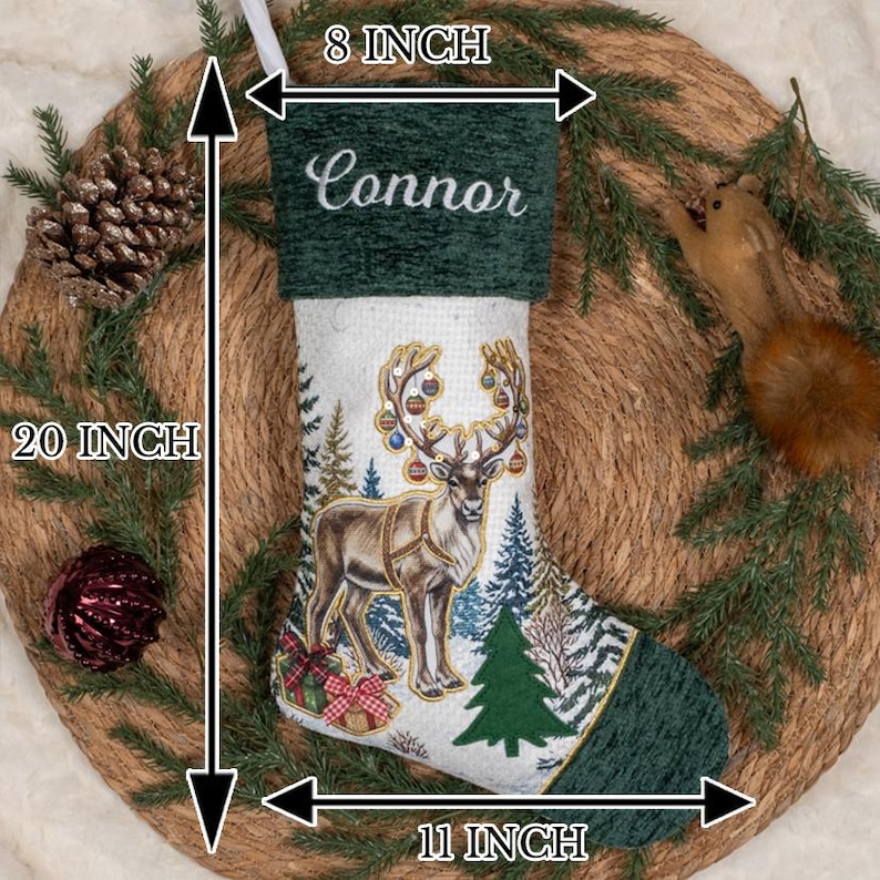 May include: A Christmas stocking measuring 50.8 cm in height, 20.3 cm at the top, and 27.9 cm at the base. It features a dark green cuff with the name Connor embroidered in white, and a white body with a reindeer, trees, and gifts.