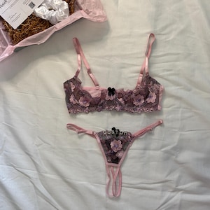May include: A pink and black floral lace lingerie set, including a bra and thong, with a small black bow. A gift box with a scrunchie and a "Thank You" card is also visible.