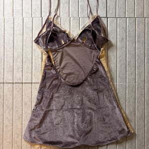 May include: A sleeveless chemise featuring a dark mauve velvet bodice with a deep scoop back and thin adjustable shoulder straps. The garment is accented with cream-colored lace trim along the neckline and side panels, creating a layered look.