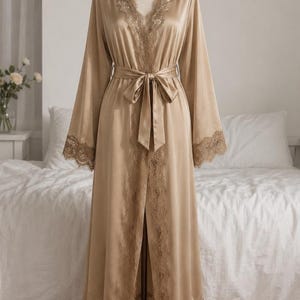 May include: A floor-length champagne-colored satin robe featuring long, wide sleeves and a V-neckline. The garment is adorned with intricate lace trim along the collar, sleeve cuffs, and hem, and includes a matching satin tie belt at the waist.
