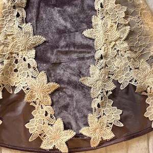 May include: A dark brown velvet garment featuring intricate cream-colored floral lace appliques along the sides. The lace design consists of detailed star-shaped flower motifs connected by delicate mesh netting, contrasting against the smooth texture.