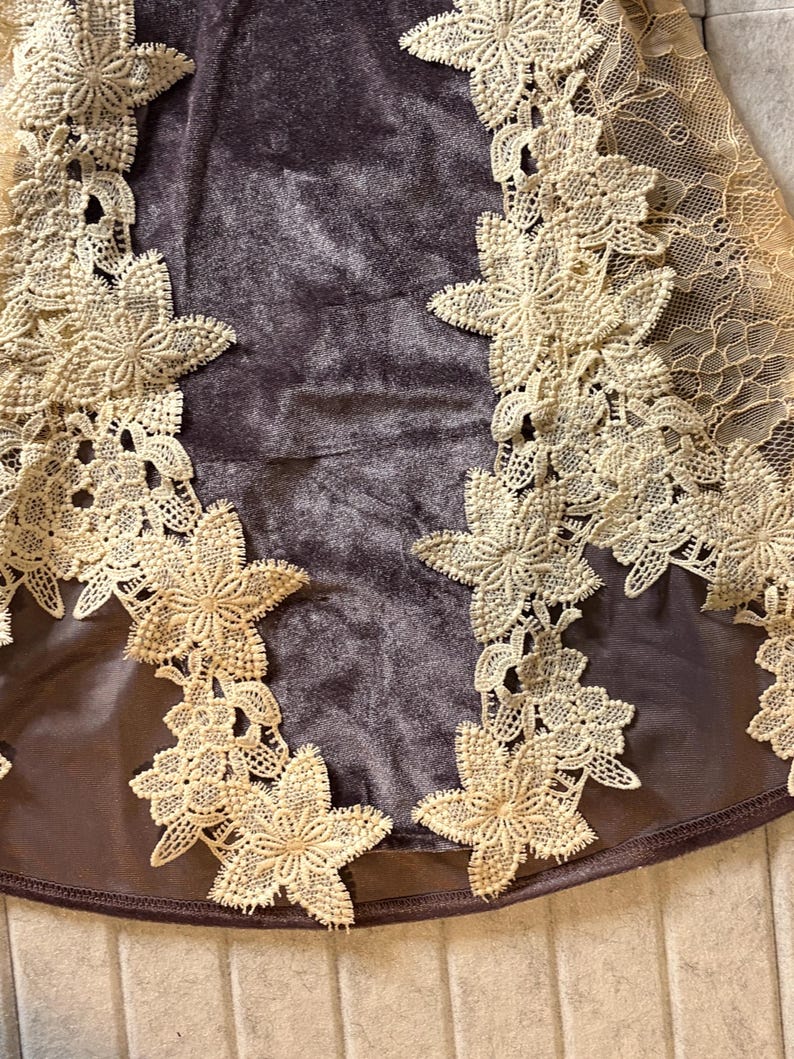 May include: A dark brown velvet garment featuring intricate cream-colored floral lace appliques along the sides. The lace design consists of detailed star-shaped flower motifs connected by delicate mesh netting, contrasting against the smooth texture.