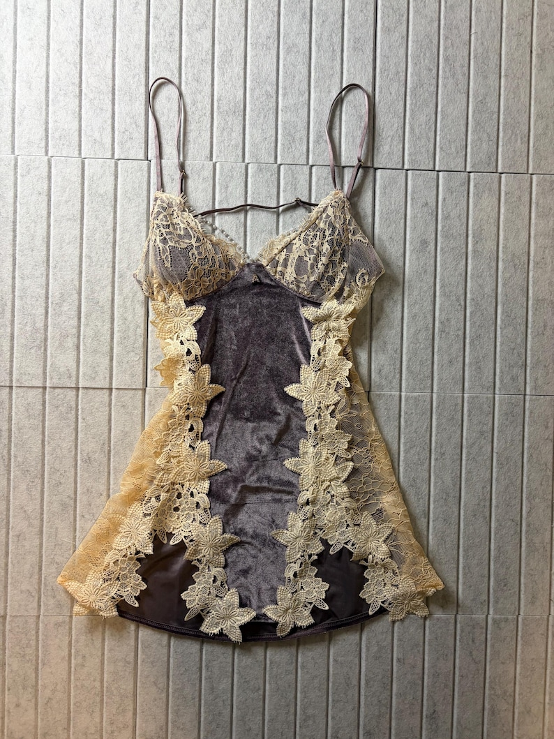 May include: A dark gray velvet chemise featuring thin adjustable shoulder straps and a V-neckline. The garment is accented with cream-colored floral lace panels along the sides and bodice, creating a layered look with a soft, textured finish.