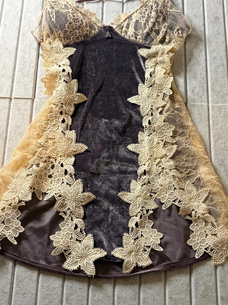 May include: A dark brown velvet slip dress featuring a deep scoop neckline and spaghetti straps. The garment is accented with wide panels of cream-colored floral lace along the sides and bodice, showcasing intricate embroidered flower motifs.