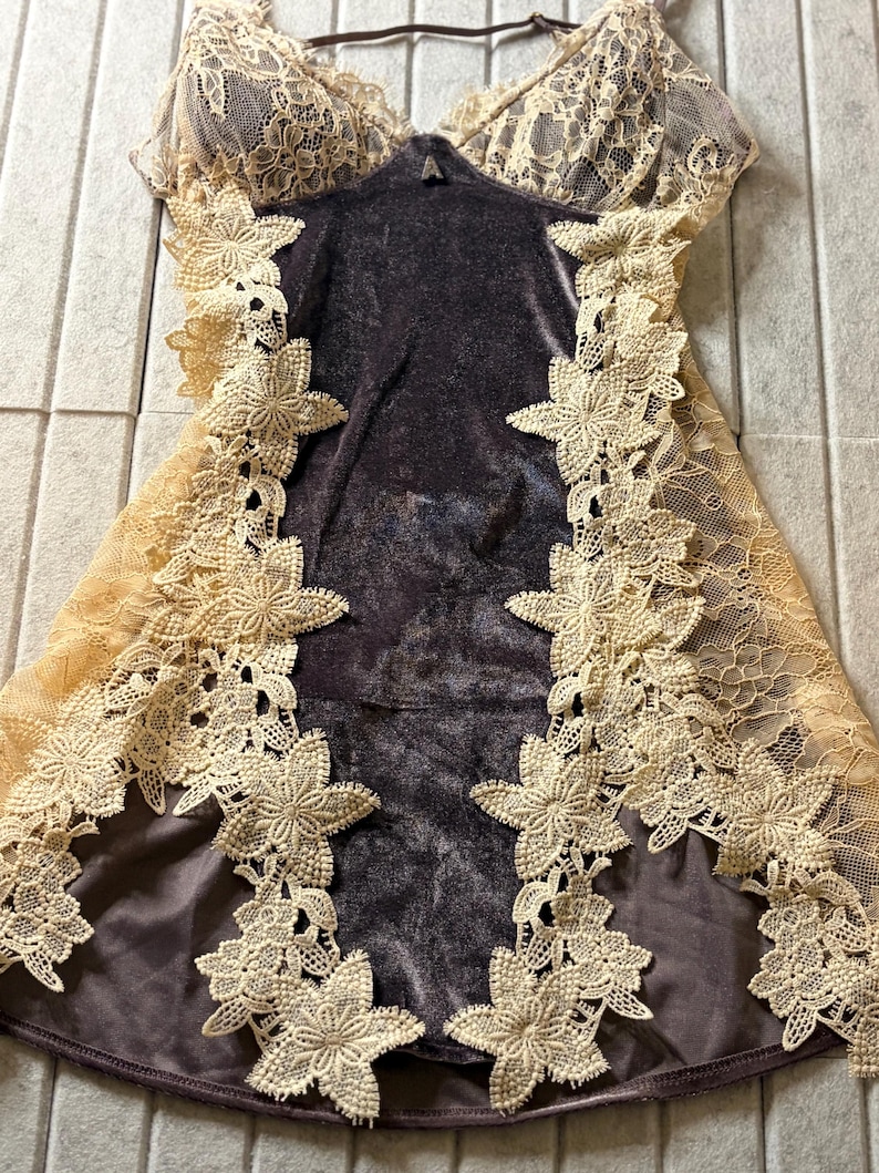 May include: A dark brown velvet camisole featuring beige lace trim along the neckline and sides. The garment is accented with vertical floral lace appliqu&eacute;s that run down the front, complemented by thin adjustable shoulder straps.