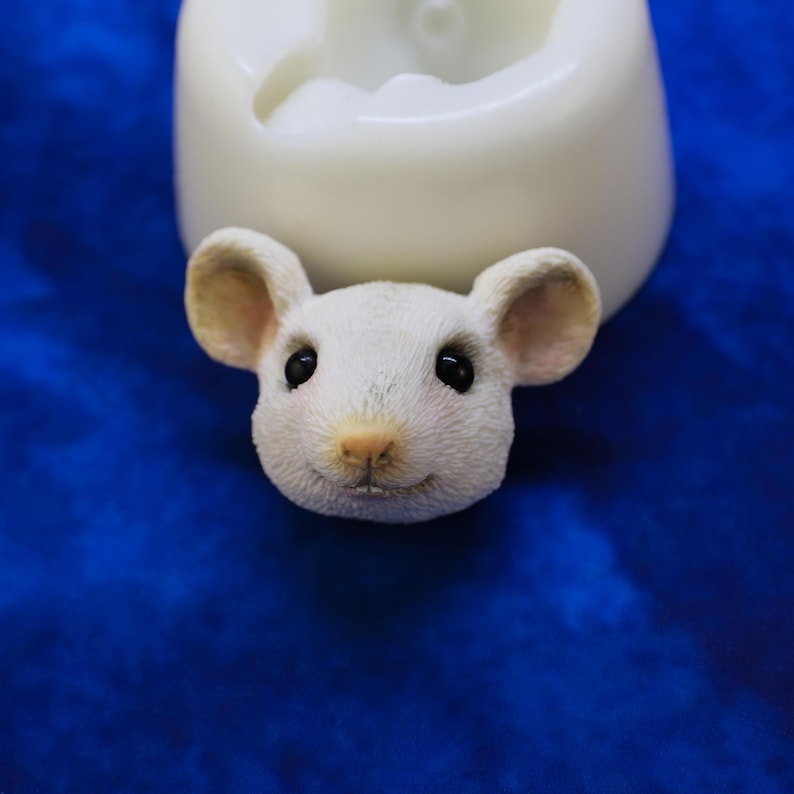 K&ouml;nnte beinhalten: Eine wei&szlig;e M&auml;usekopf-Figur mit gro&szlig;en Ohren, schwarzen Augen und einer rosa Nase. Die Maus l&auml;chelt. Im Hintergrund befindet sich eine wei&szlig;e Form. Die Figur ist wahrscheinlich f&uuml;r Bastelarbeiten oder Dekoration gedacht.