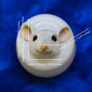 Peut inclure: Figurine de souris blanche avec des yeux noirs et un nez rose, montée sur une base circulaire blanche. La souris mesure 25 mm de large, 22 mm de haut et 28 mm de haut avec les oreilles. La longueur est de 25 mm.
