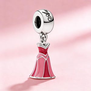 Op de afbeelding: Een zilveren bedel met het woord "Aurora" in script. De bedel heeft een roze en rode jurk ontwerp, met een zilveren balein. De bedel is opgehangen aan een zilveren ring.