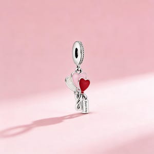 以下が含まれることがあります： 白、ピンク、赤のハート型の風船が3つ付いたシルバーチャーム。チャームには「Happy Day」と書かれた小さなタグが付いています。チャームの上部には、小さな透明な石が付いたループがあります。