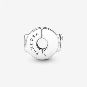 May include: A silver-colored charm with a circular design, split into two halves. The word "PANDORA" is engraved on one half. The charm has a small hole in the center and two small protrusions on either side. The background is plain white.