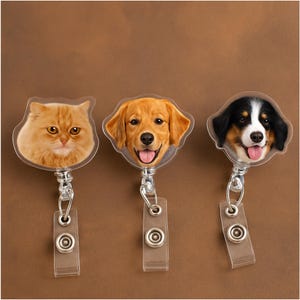 Puede incluir: Tres portatarjetas retráctiles con caras de animales: un gato naranja, un golden retriever y un boyero de Berna. Cada carrete de insignia tiene un clip de plástico transparente y un carrete de metal plateado.