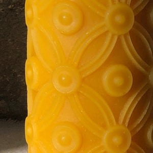 May include: A yellow candle with a repeating pattern of circles and flower shapes.