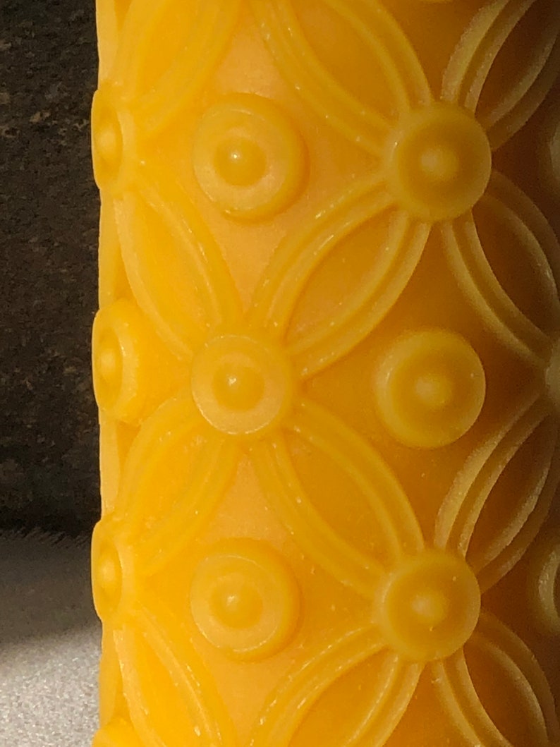 May include: A yellow candle with a repeating pattern of circles and flower shapes.