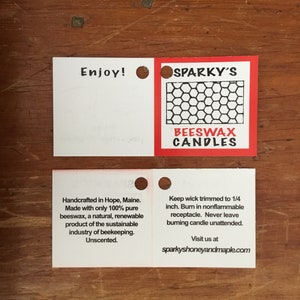 May include: Two white square labels with rounded corners. The top label says "Enjoy!" and has a hole punched in the upper right corner. The bottom label says "Handcrafted in Hope, Maine. Made with only 100% pure beeswax, a natural, renewable product of the sustainable industry of beekeeping. Unscented."