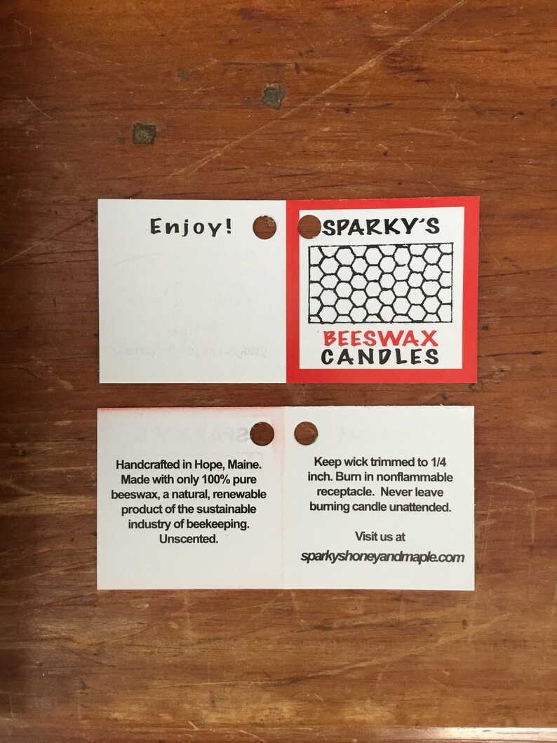 May include: Two white square labels with rounded corners. The top label says "Enjoy!" and has a hole punched in the upper right corner. The bottom label says "Handcrafted in Hope, Maine. Made with only 100% pure beeswax, a natural, renewable product of the sustainable industry of beekeeping. Unscented."
