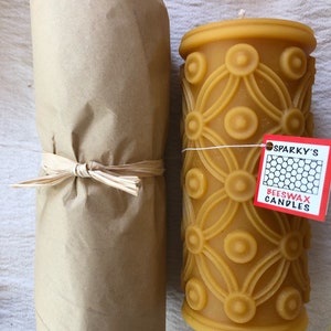 May include: A brown paper wrapped beeswax candle with a decorative pattern and a red label that says "Sparky's Beeswax Candles".
